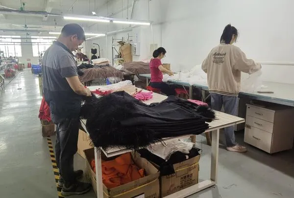 Factory workers conducting quality inspection and packing on feather-trimmed bandage dresses.